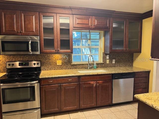 kitchen with light stone counters, a sink, appliances with stainless steel finishes, decorative backsplash, and glass insert cabinets