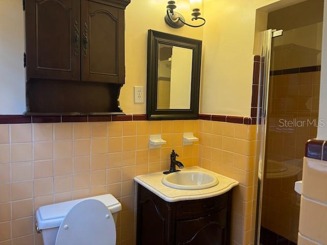 full bath with tile walls, toilet, wainscoting, a shower stall, and vanity