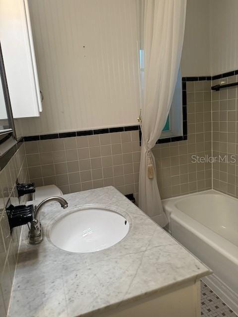 full bathroom featuring a wainscoted wall, shower / bathtub combination with curtain, tile walls, and a sink