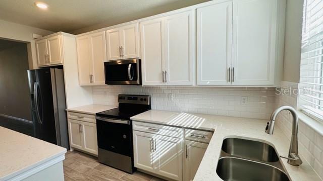 kitchen featuring backsplash, black appliances, sink, and white cabinetry