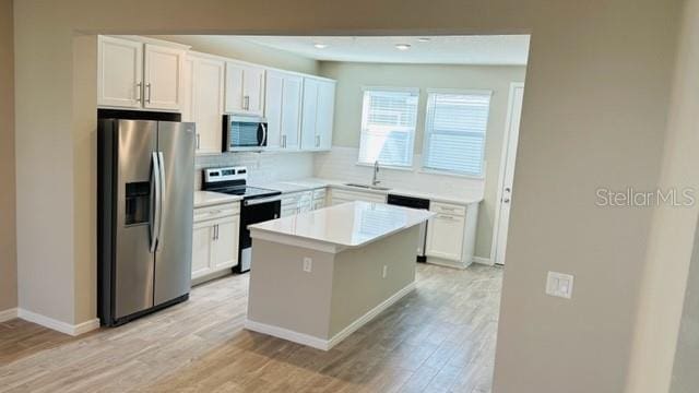 kitchen featuring a kitchen island, light wood-type flooring, decorative backsplash, stainless steel appliances, and white cabinetry