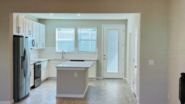 kitchen with a kitchen island, stainless steel appliances, tasteful backsplash, light hardwood / wood-style floors, and white cabinetry