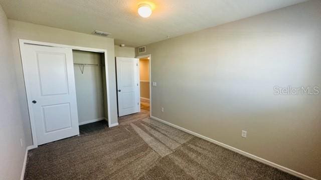 unfurnished bedroom with dark carpet and a closet