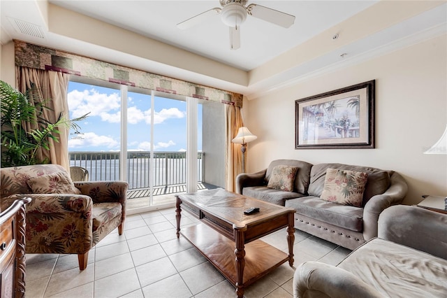 living room with ceiling fan, a tray ceiling, and light tile patterned flooring