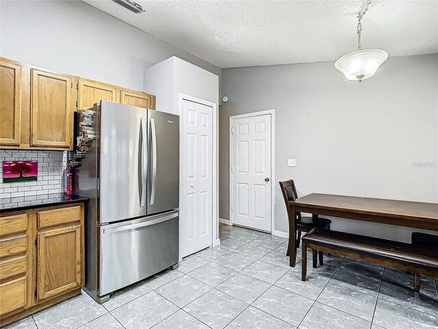 kitchen featuring a textured ceiling, vaulted ceiling, pendant lighting, backsplash, and stainless steel refrigerator