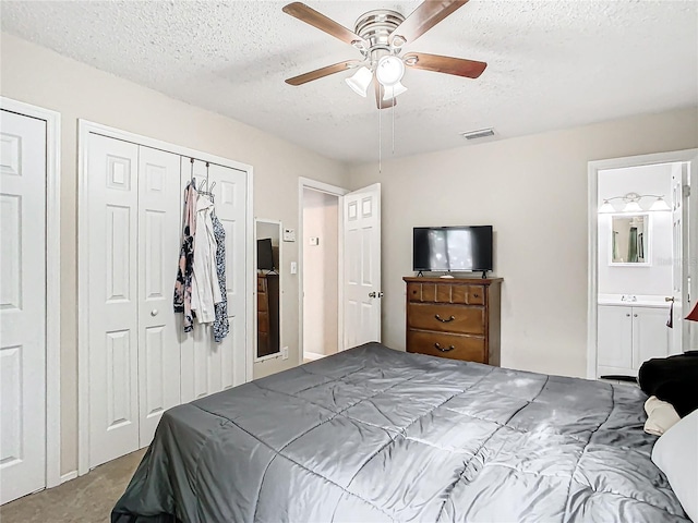 bedroom featuring carpet floors, a textured ceiling, ceiling fan, two closets, and ensuite bathroom