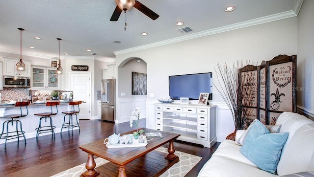 living room with a textured ceiling, ceiling fan, ornamental molding, and dark hardwood / wood-style flooring