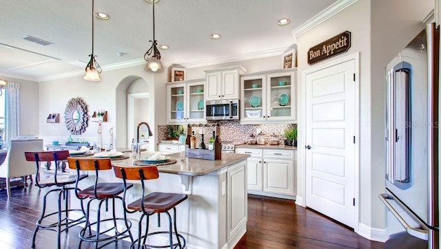 kitchen with dark hardwood / wood-style floors, appliances with stainless steel finishes, a kitchen island with sink, hanging light fixtures, and white cabinetry