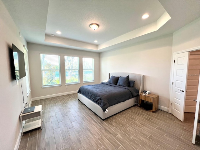 bedroom with wood finish floors, a raised ceiling, baseboards, and recessed lighting