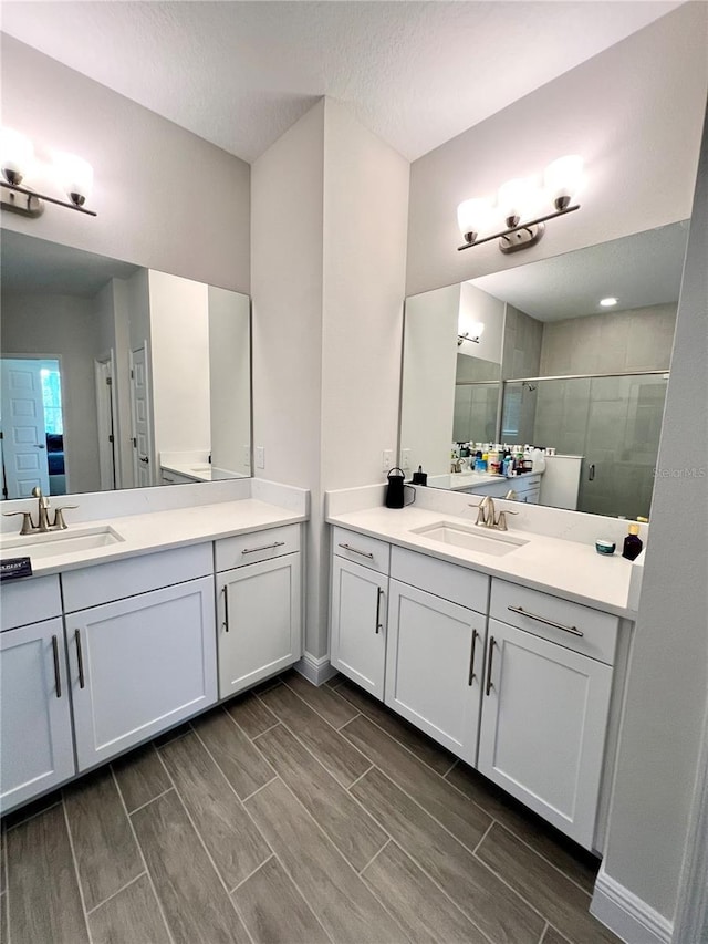 full bath with wood finish floors, a stall shower, two vanities, and a sink