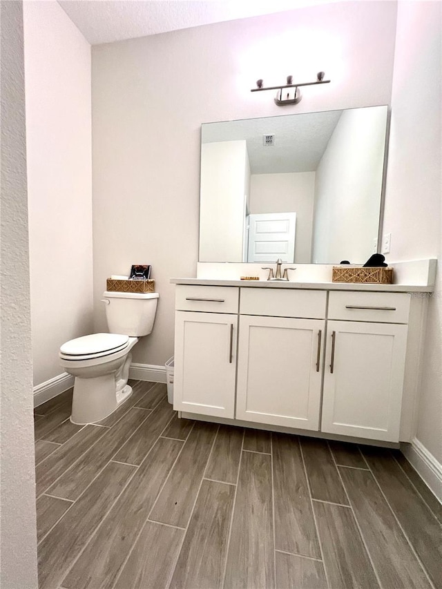 bathroom with wood tiled floor, baseboards, vanity, and toilet