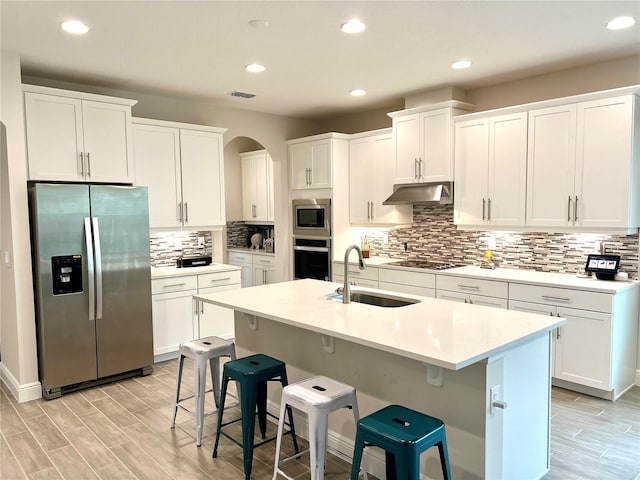 kitchen with arched walkways, visible vents, appliances with stainless steel finishes, a sink, and under cabinet range hood