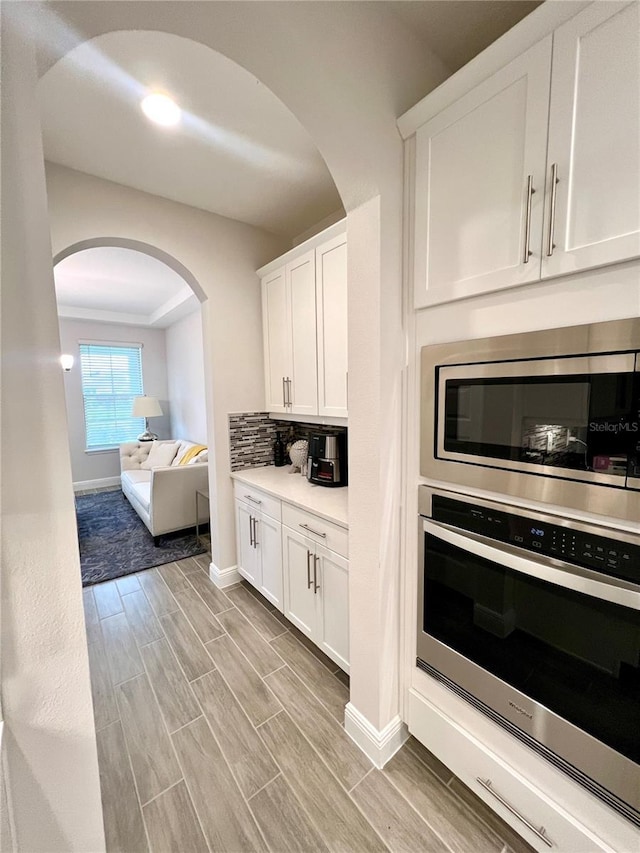 kitchen with stainless steel appliances, decorative backsplash, wood tiled floor, white cabinets, and baseboards