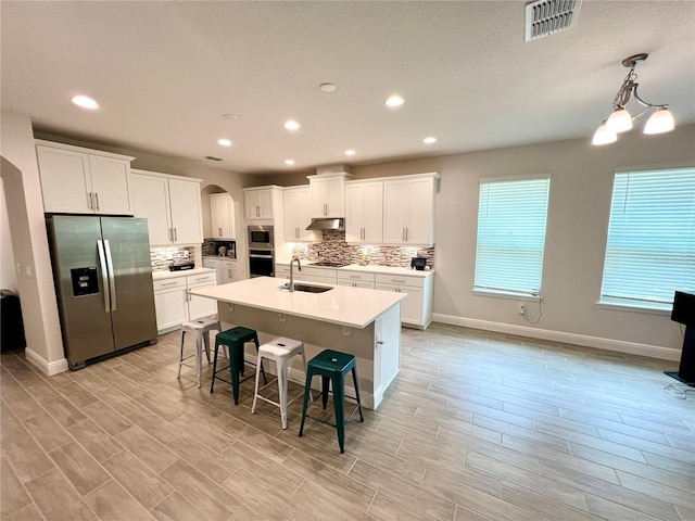 kitchen featuring arched walkways, under cabinet range hood, stainless steel appliances, a sink, and visible vents