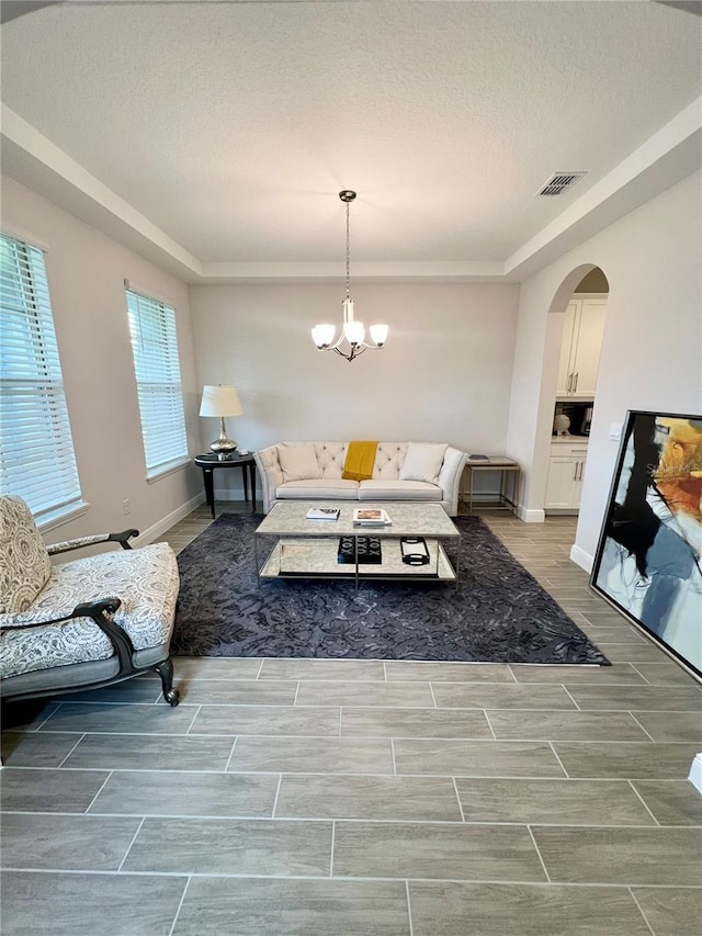 living room featuring arched walkways, wood finish floors, visible vents, a chandelier, and baseboards