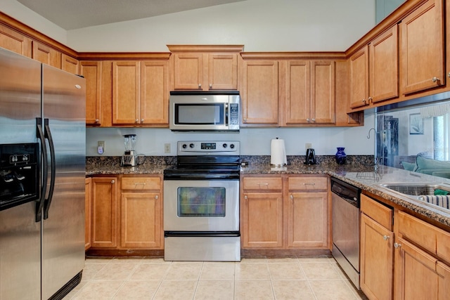 kitchen with light tile patterned flooring, lofted ceiling, appliances with stainless steel finishes, and dark stone counters