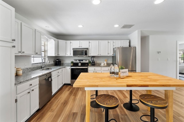 kitchen featuring light stone counters, stainless steel appliances, sink, white cabinets, and light hardwood / wood-style flooring