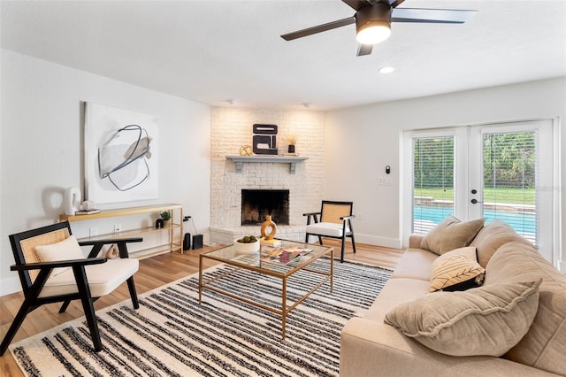 living room with french doors, hardwood / wood-style floors, ceiling fan, and a brick fireplace