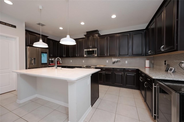 kitchen with appliances with stainless steel finishes, a kitchen island with sink, wine cooler, light tile patterned flooring, and decorative light fixtures