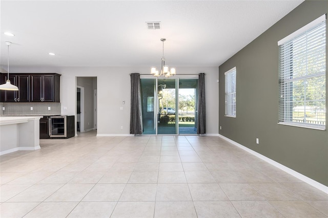 unfurnished living room featuring a wealth of natural light, beverage cooler, a chandelier, and light tile patterned floors