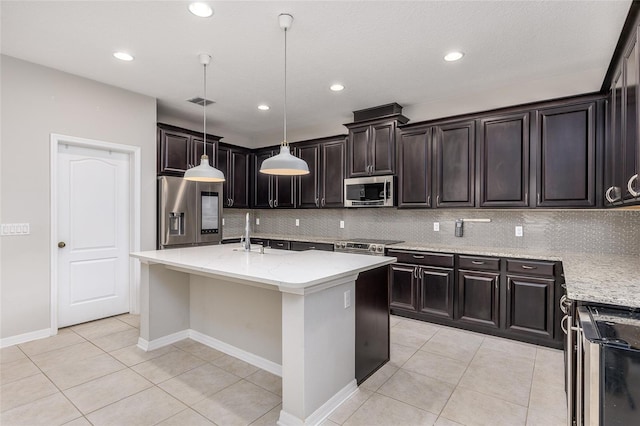 kitchen featuring hanging light fixtures, light tile patterned floors, stainless steel appliances, and an island with sink