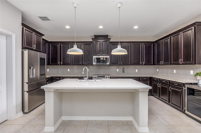 kitchen featuring light tile patterned flooring, dark brown cabinetry, a center island with sink, appliances with stainless steel finishes, and pendant lighting