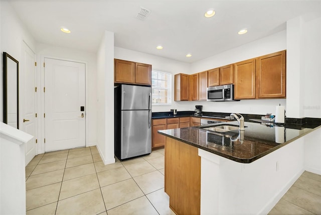 kitchen with appliances with stainless steel finishes, sink, dark stone counters, light tile patterned flooring, and kitchen peninsula