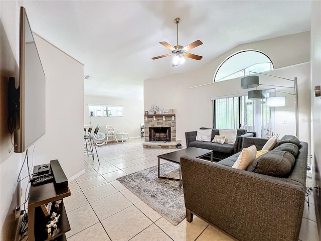 tiled living room with ceiling fan, plenty of natural light, vaulted ceiling, and a stone fireplace