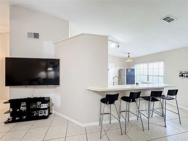 kitchen featuring a textured ceiling, vaulted ceiling, light tile patterned floors, stainless steel refrigerator, and sink