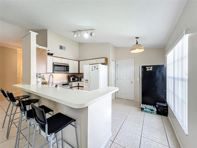 kitchen featuring lofted ceiling, kitchen peninsula, white refrigerator with ice dispenser, and fridge