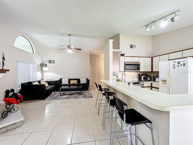 kitchen with light tile patterned floors, white refrigerator with ice dispenser, kitchen peninsula, ceiling fan, and a textured ceiling