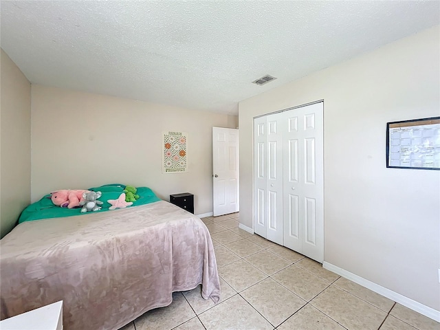 bedroom featuring a textured ceiling, light tile patterned floors, and a closet