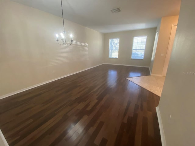 unfurnished room featuring dark wood-type flooring and a notable chandelier