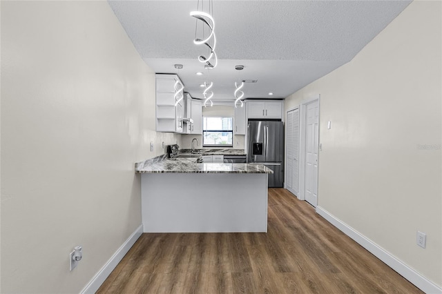 kitchen featuring hardwood / wood-style floors, light stone counters, kitchen peninsula, stainless steel fridge with ice dispenser, and a textured ceiling