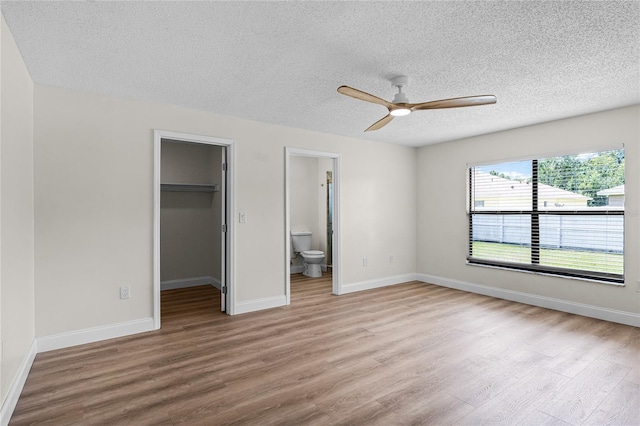 unfurnished bedroom featuring a walk in closet, a closet, ensuite bath, ceiling fan, and light wood-type flooring