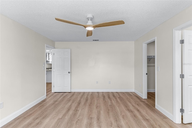 unfurnished bedroom with light wood-type flooring, a walk in closet, a closet, ceiling fan, and a textured ceiling