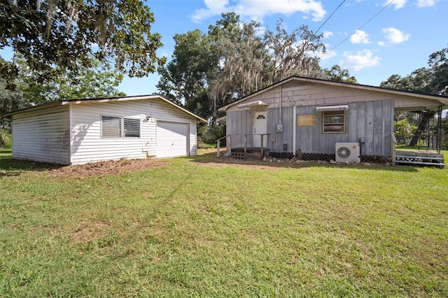 rear view of property featuring ac unit, a garage, a lawn, and an outbuilding