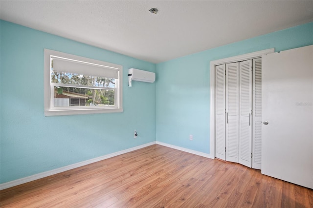 unfurnished bedroom featuring a wall mounted AC, wood-type flooring, and a closet