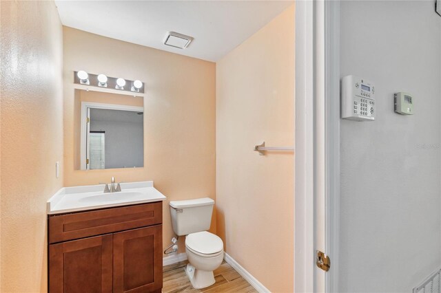 bathroom featuring visible vents, baseboards, toilet, wood finished floors, and vanity