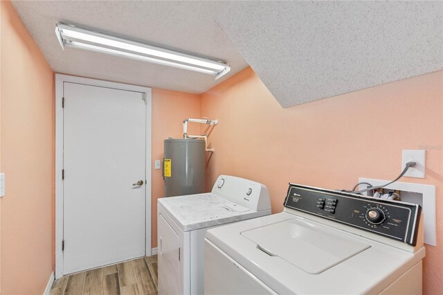 clothes washing area with water heater, light wood-style flooring, a textured ceiling, separate washer and dryer, and laundry area