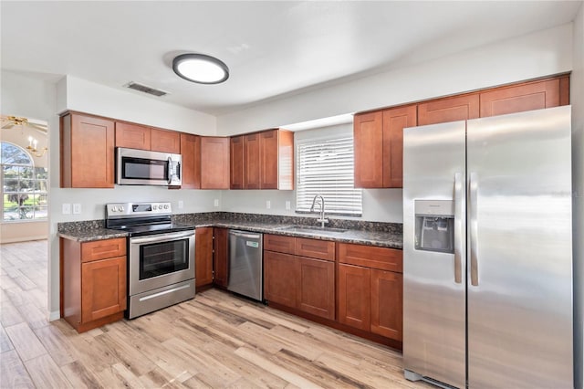 kitchen featuring light hardwood / wood-style flooring, appliances with stainless steel finishes, dark stone countertops, and sink