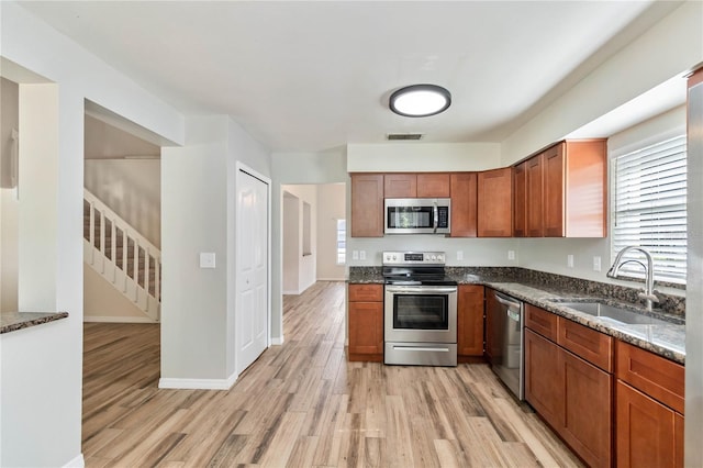 kitchen featuring light wood-type flooring, dark stone countertops, stainless steel appliances, and sink