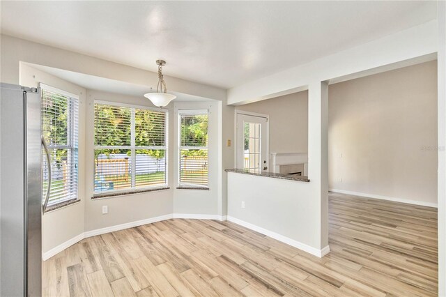 unfurnished dining area with a healthy amount of sunlight, light wood-style flooring, a fireplace, and baseboards