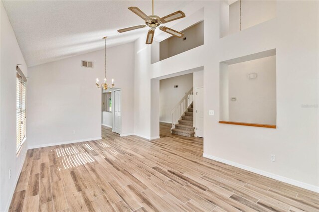 unfurnished room featuring visible vents, stairway, a textured ceiling, light wood-type flooring, and ceiling fan with notable chandelier