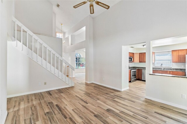 unfurnished living room featuring light wood finished floors, stairs, baseboards, and a ceiling fan