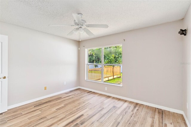 empty room with a textured ceiling, wood finished floors, a ceiling fan, and baseboards