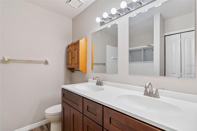 bathroom featuring double vanity, baseboards, toilet, and a sink