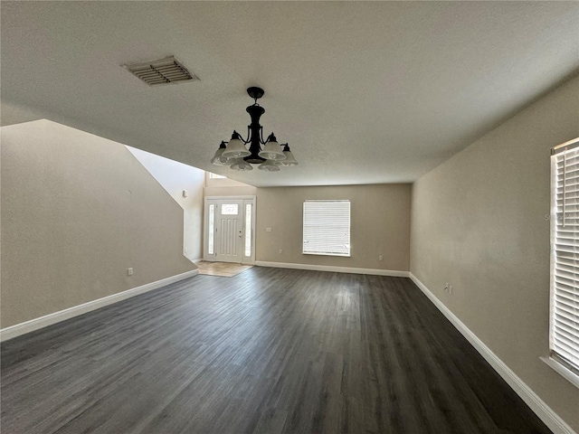 interior space featuring dark hardwood / wood-style flooring, vaulted ceiling, a chandelier, and a textured ceiling