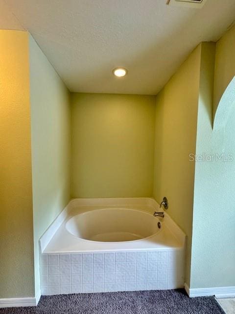 bathroom featuring a textured ceiling and a relaxing tiled tub