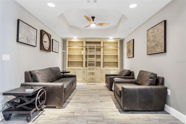 living room with light wood-type flooring, a raised ceiling, and ceiling fan